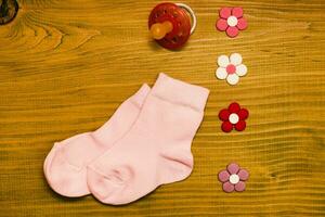 poco rosa bambino ragazza calzini con pacificatore e fiori su di legno tavolo.bambino annuncio concetto. foto
