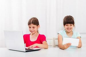 carino poco ragazze siamo seduta e utilizzando il computer portatile e digitale tavoletta. foto