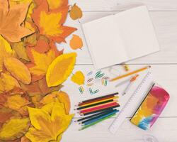 autunno foglie, matite, taccuino, scuola forniture, e un' taccuino su un' bianca di legno foto