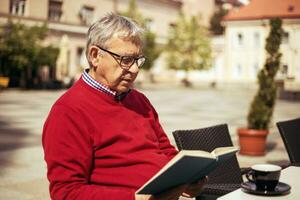 anziano uomo gode lettura libro e potabile caffè a il bar foto