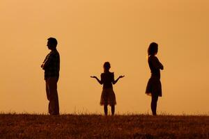 silhouette di un' arrabbiato marito e moglie su ogni altro con loro confuso figlia in piedi nel il mezzo foto