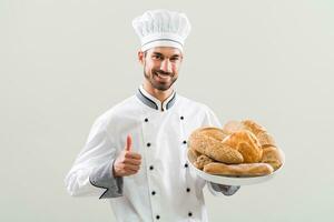 panettiere Tenere mazzo di pane e mostrando pollice su su grigio sfondo. foto