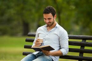 giovane uomo d'affari gode è su un' caffè rompere e lui gode lettura un' libro e seduta a il parco foto