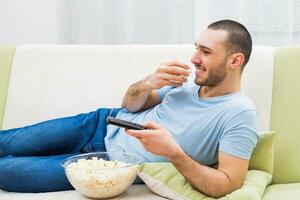 giovane uomo gode Guardando tv e mangiare Popcorn foto