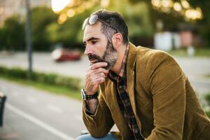 depresso uomo d'affari con barba seduta su il panchina nel il città foto