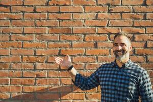 ritratto di moderno uomo d'affari con barba Esprimere a gesti mentre in piedi nel davanti di mattone parete all'aperto foto