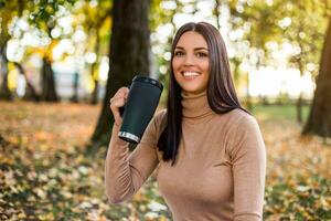 bellissimo donna potabile caffè mentre gode nel autunno nel il parco foto