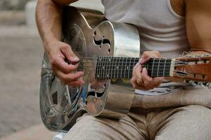 un' uomo giocando un acustico chitarra su il strada foto