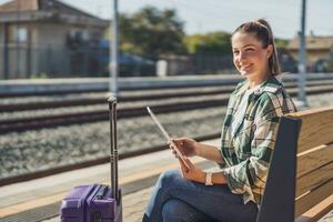contento donna utilizzando digitale tavoletta mentre in attesa per sua treno su un' Ferrovia stazione foto