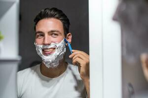 uomo rasatura barba mentre guardare lui stesso nel il specchio foto