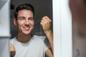 uomo è utilizzando dentale filo mentre guardare lui stesso nel il specchio foto
