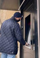 uomo nel un' nero maschera e un' monouso guanto usi un ATM. selettivo messa a fuoco foto