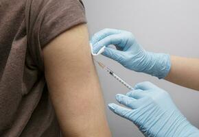 mani di un' medico lavoratore nel blu nitrile guanti Tenere un' siringa con un' vaccino vicino il del paziente spalla. selettivo fuoco.alto qualità foto