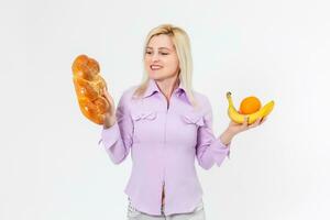 giovane bellissimo e contento ragazza con lungo capelli detiene banane su sua giusto mano e un' ciambella su sua sinistra mano, isolato al di sopra di bianca sfondo foto