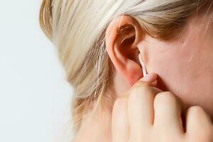 bionda donna pulisce sua orecchio con un' bianca cotone tampone vicino su foto