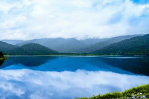 bellissimo paesaggio con montagne drammatico lago nel il nebbia riflessione di cielo e nube nel acqua foto