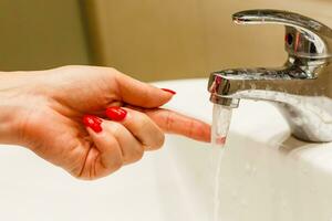 avvicinamento su dita vicino rubinetto di Lavello o vasca da bagno nel casa bagno. femmina a casa controllo in esecuzione acqua toccante con mano foto