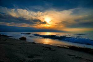 tramonto su il ovest spiaggia su il baltico mare. onde, spiaggia, nuvoloso cielo e luce del sole foto