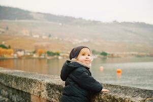 all'aperto ritratto di adorabile bambino piccolo ragazza giocando di il lago su un' freddo autunno giorno, indossare caldo giacca e cappello foto