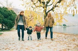 all'aperto ritratto di giovane contento famiglia di quattro, madre e padre giocando con bambini nel autunno parco di il lago, freddo tempo metereologico foto