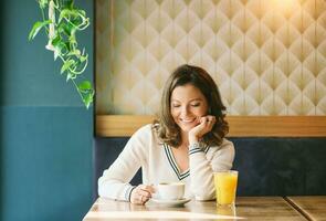 ritratto di contento salutare donna avendo caffè e arancia succo nel bar foto