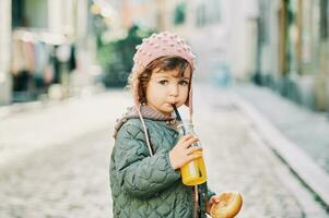 all'aperto ritratto di carino bambino piccolo ragazza Tenere latte pane panino, potabile arancia succo a partire dal il bottiglia foto