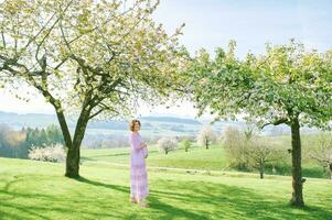 all'aperto ritratto di contento incinta donna godendo simpatico soleggiato giorno nel primavera giardino foto