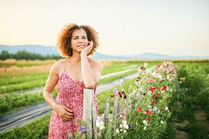 all'aperto ritratto di bellissimo mezzo età donna godendo simpatico suuny sera nel campagna, pendente su fiore recinzione, indossare rosso vestito foto