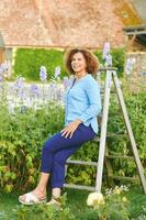 all'aperto ritratto di bellissimo 50 anno vecchio donna godendo simpatico giorno nel fiore parco o giardino, contento e salutare stile di vita foto