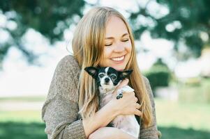 all'aperto ritratto di contento giovane donna abbracciare piccolo chihuahua nero e bianca cane foto