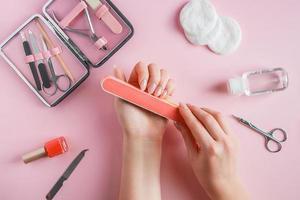 la donna fa una manicure a casa. mani con una lima per unghie su sfondo rosa. foto