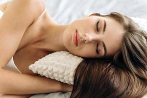 riposando a letto. ritratto dell'attraente giovane donna sdraiata con le mani sotto il cuscino e tenendo gli occhi chiusi con umore pacifico foto