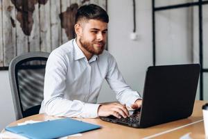 uomo serio e barbuto che lavora al computer in ufficio foto