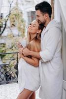 marito abbraccia la moglie incinta in accappatoio sul balcone foto