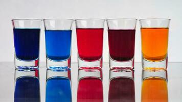 piccolo bicchieri pieno con colorato acqua siamo ordinatamente disposte su un isolato bianca sfondo foto