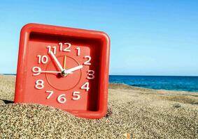 un' rosso orologio su il spiaggia con il oceano nel il sfondo foto