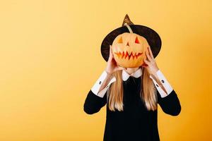 donna in piedi su uno sfondo giallo che tiene in mano una zucca e nasconde il viso foto