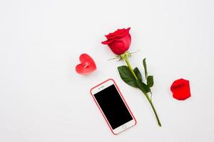 una rosa rosso scuro e un telefono cellulare isolati su sfondo bianco foto