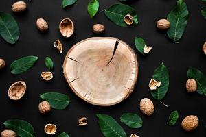 guscio di noce e foglie verdi fresche sparse su uno sfondo nero. taglio di legno dell'albero al centro foto