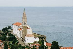 santo Giorgio Cattedrale nel pirano con calma mare su il sfondo e verde alberi nelle vicinanze foto