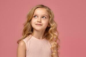 poco ragazza con un' biondo Riccio capelli, nel un' rosa vestito è in posa per il telecamera foto