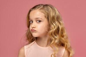 poco ragazza con un' biondo Riccio capelli, nel un' rosa vestito è in posa per il telecamera foto