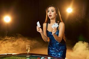 giovane bellissimo donna pose vicino poker tavolo nel lusso casinò. passione, carte, patatine fritte, alcol, dado, gioco d'azzardo, casinò - esso è come femmina intrattenimento. Fumo sfondo. foto