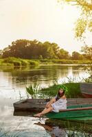 giovane donna con fiore ghirlanda su sua testa, rilassante su barca su fiume a tramonto. concetto di femmina bellezza, riposo nel il villaggio foto