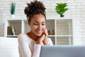 donna carina guardando lo schermo del computer portatile seduto in ufficio e sorridendo dolcemente. - Immagine foto