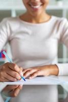 primo piano che ritaglia l'immagine con la ragazza durante la scrittura con la penna su un foglio, donna d'affari che firma un documento foto