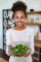 bella donna a casa che mostra cibo sano, tiene tra le mani un'insalata - immagine foto