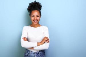 felice donna afroamericana con le braccia conserte mentre sta in piedi su sfondo blu studio- immagine foto