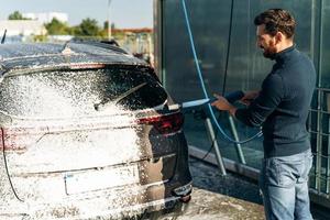 lavaggio auto dal suo proprietario caucasico. vista posteriore dell'uomo che pulisce la sua automobile con acqua ad alta pressione in strada durante l'estate foto