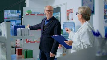 anziano uomo nel farmacia guardare a digitale pubblicità su tv schermo, interessato nel Prodotto mostrato. utile farmacista nel farmacista consigliare cliente ideale medicamento foto